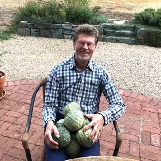 A grower seated with a lapful of freshly harvested squash