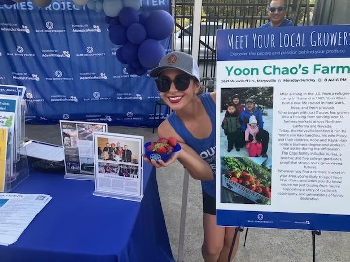 A partner at the Blue Zones Project booth sharing a Meet Your Local Growers display